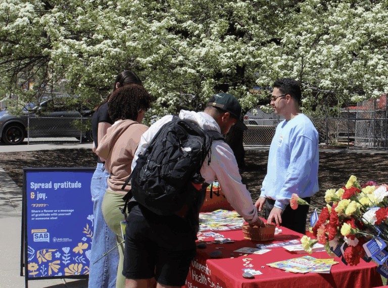 Three students taking items off a table at a mental health event. A mental health student advisory board member is on the opposite side of the table.